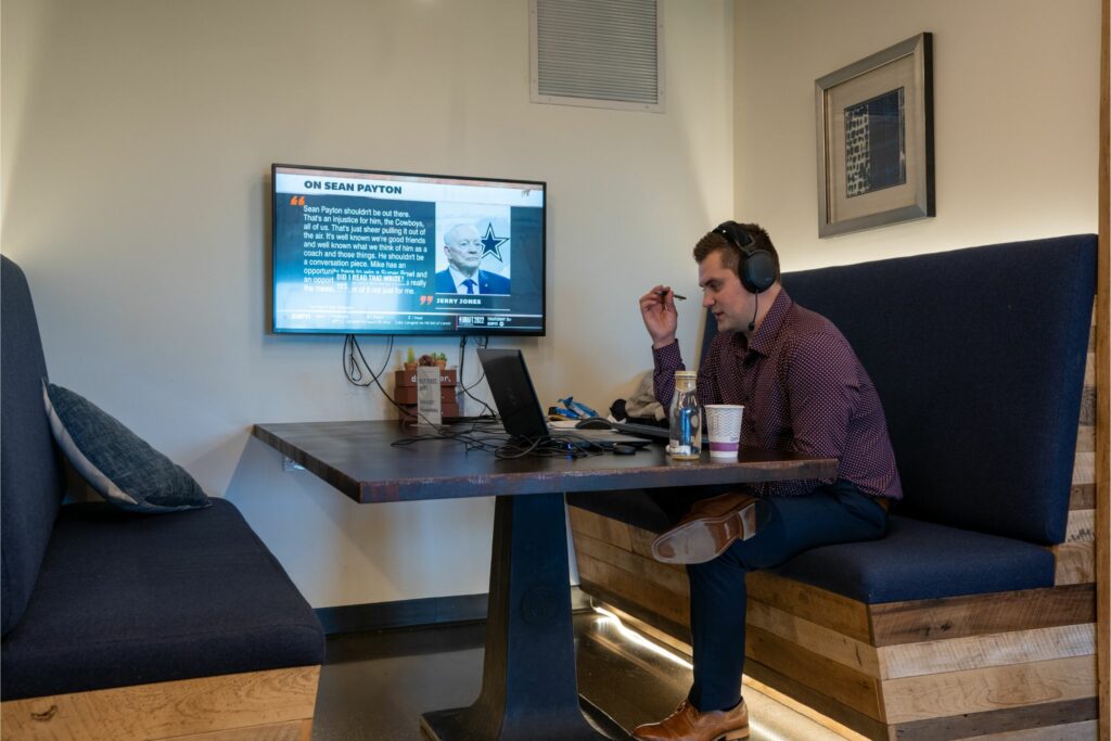 Professional working in a cozy coworking space booth, using a laptop with a tv screen in the background