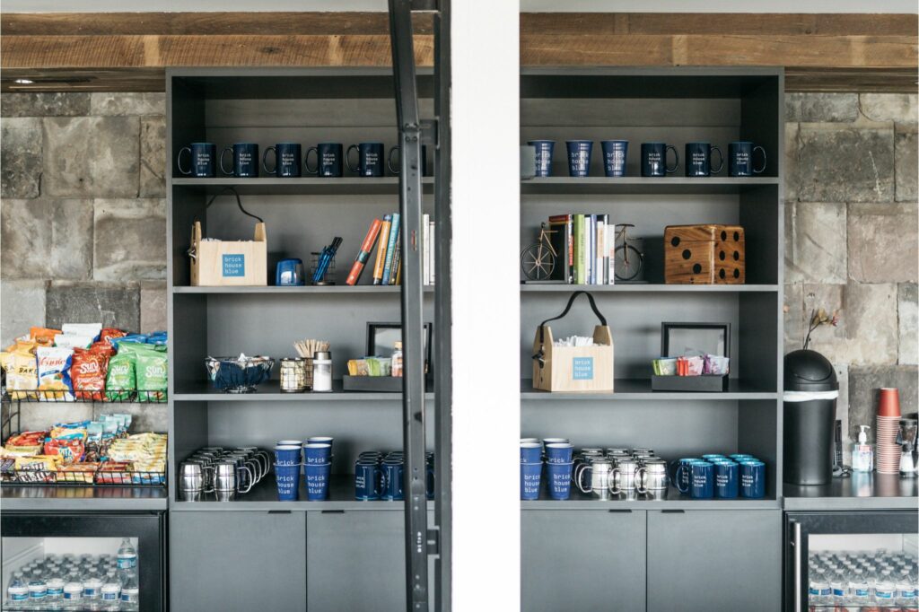 Coworking space snack bar with a variety of snacks, beverages, and branded mugs on display.