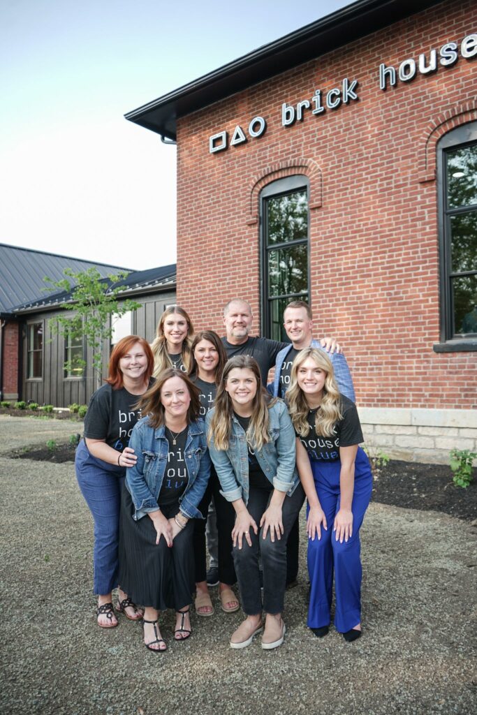 Team members standing outside a coworking space, smiling and wearing matching brick house blue shirts.